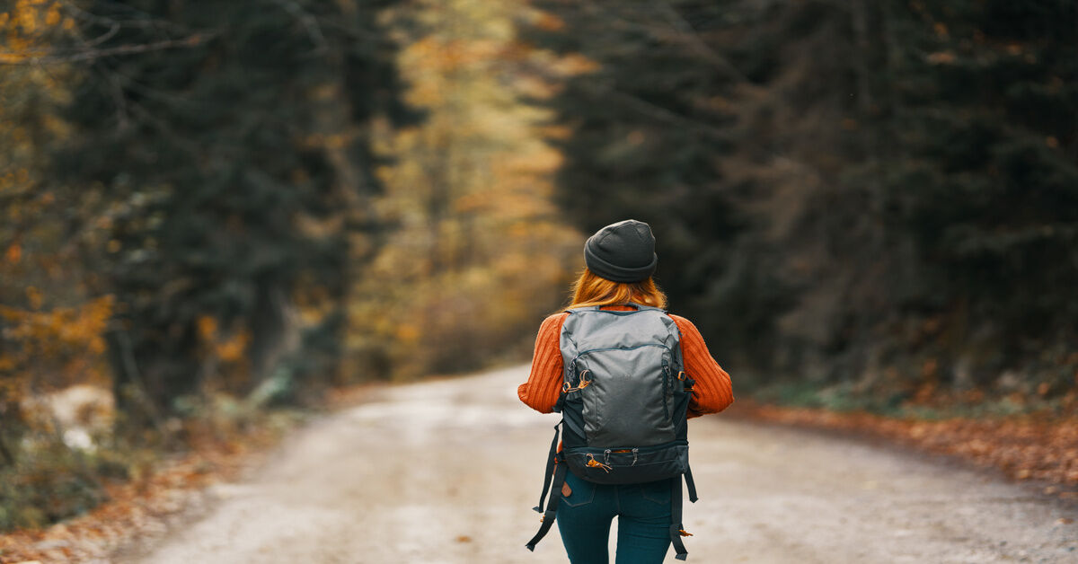 A behind shot of a traveler wearing an orange sweater, a black beanie, and a black rucksack. A behind shot of a traveler wearing an orange sweater, a black beanie, and a black rucksack.