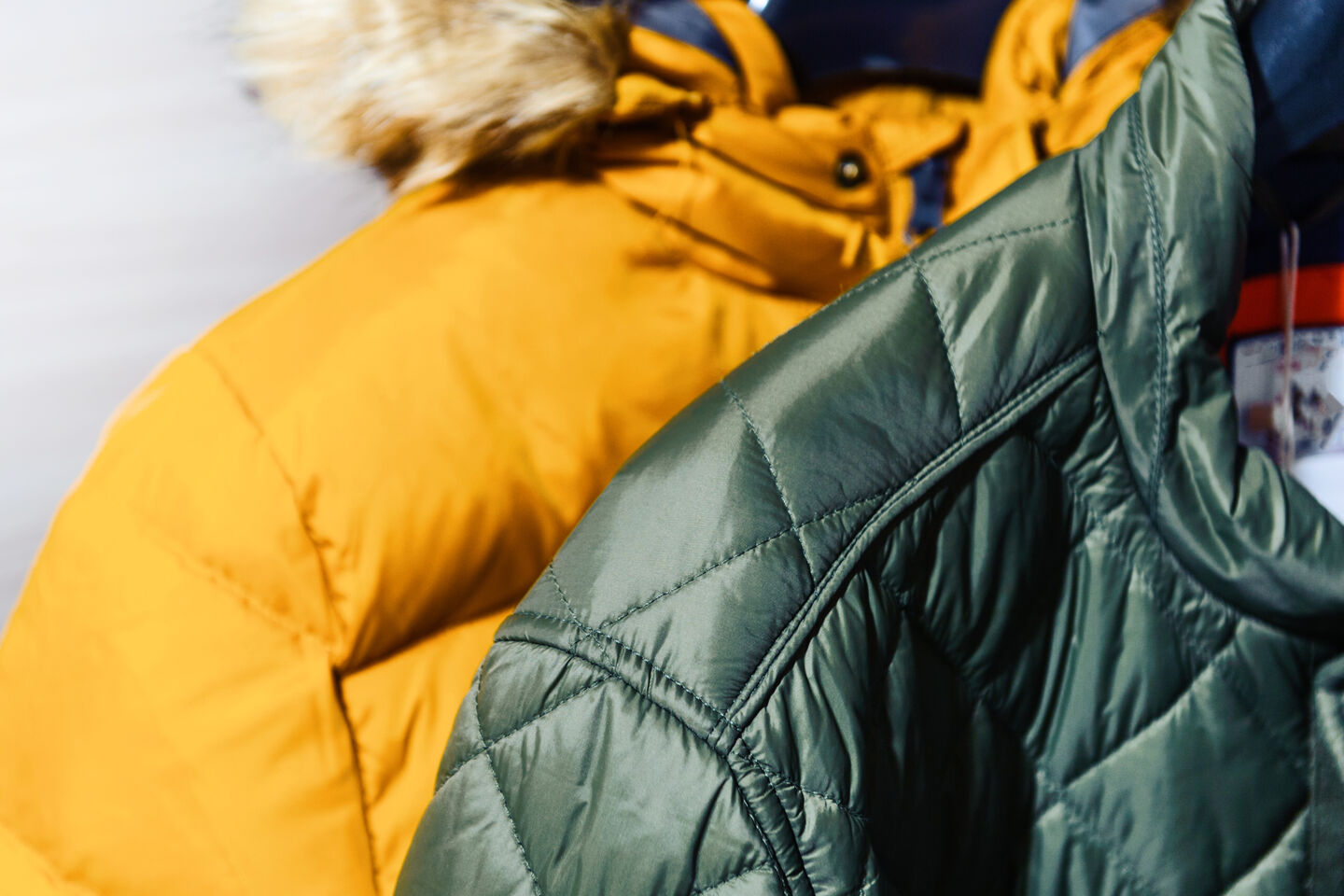 A close-up of two down jackets. The yellow one has a fur lining on the hood, while the green one does not.