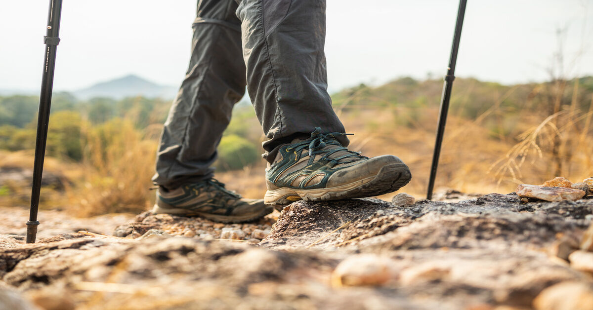 A close-up of a person wearing mountain boots and using trekking poles to cross a rocky terrain. A close-up of a person wearing mountain boots and using trekking poles to cross a rocky terrain.